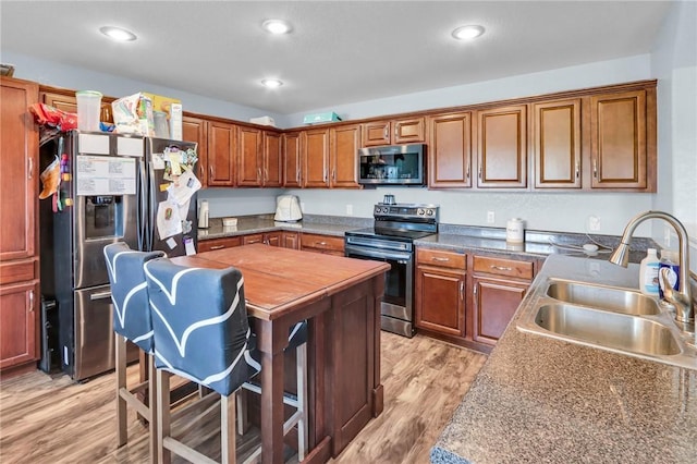 kitchen with stainless steel appliances, sink, dark stone counters, and light hardwood / wood-style flooring