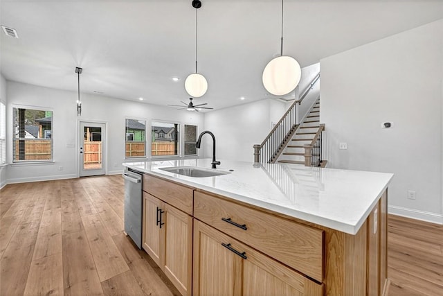 kitchen featuring pendant lighting, sink, a kitchen island with sink, stainless steel dishwasher, and light wood-type flooring