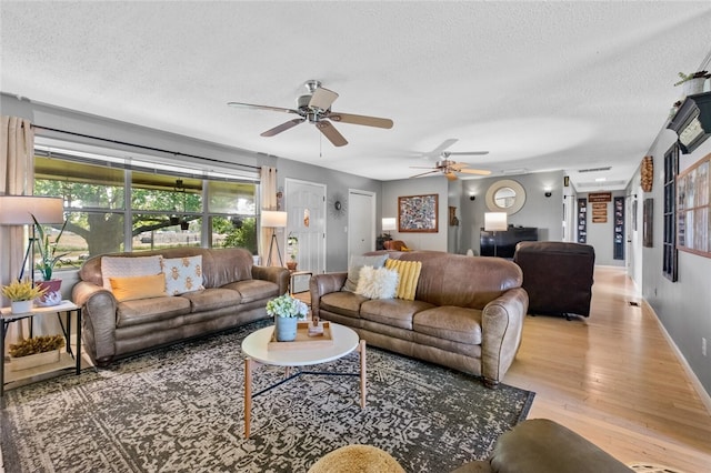 living room with a textured ceiling, light wood-type flooring, and ceiling fan