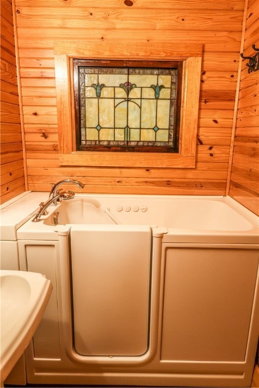 bathroom with a bath, washer and clothes dryer, and wood walls