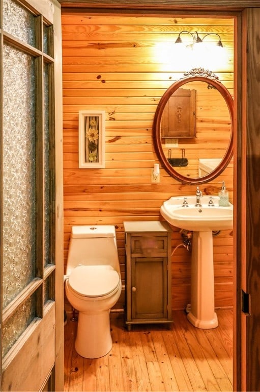 bathroom with wood-type flooring, wood walls, and toilet