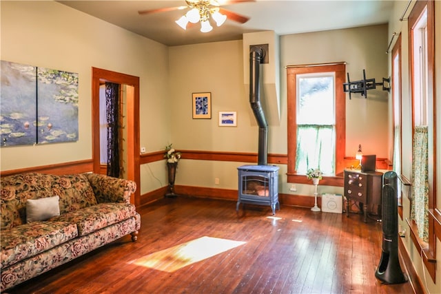 living area featuring dark hardwood / wood-style flooring, ceiling fan, and a wood stove