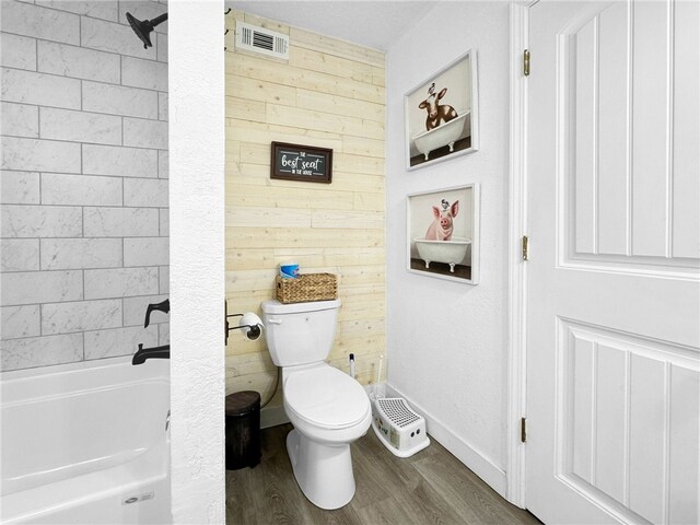 bathroom featuring wood-type flooring, wooden walls, washtub / shower combination, and toilet