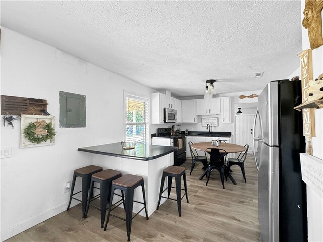 kitchen with appliances with stainless steel finishes, electric panel, light hardwood / wood-style flooring, white cabinets, and kitchen peninsula