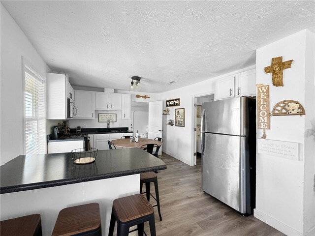 kitchen with hardwood / wood-style floors, appliances with stainless steel finishes, white cabinetry, a kitchen bar, and kitchen peninsula