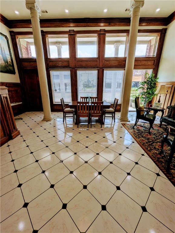 tiled dining space with ornamental molding, ornate columns, and a high ceiling