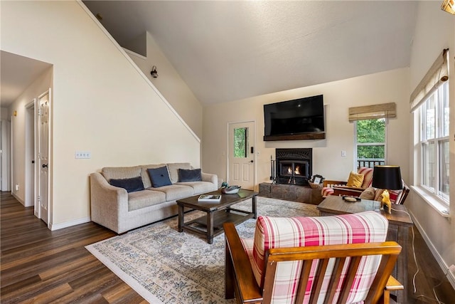 living room featuring high vaulted ceiling, dark wood finished floors, baseboards, and a warm lit fireplace
