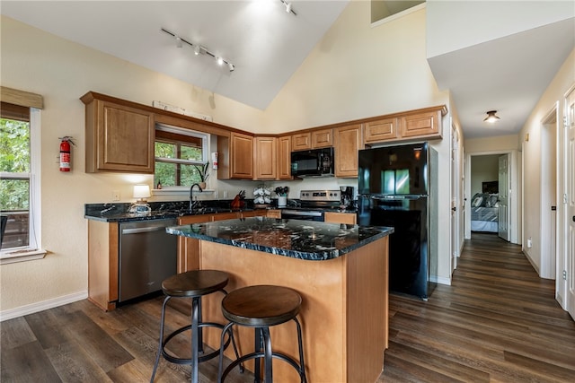 kitchen featuring dark hardwood / wood-style flooring, a center island, dark stone counters, and black appliances