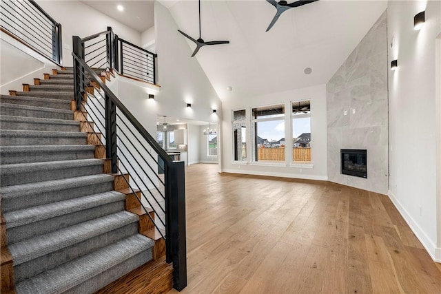 staircase with hardwood / wood-style flooring, ceiling fan, a premium fireplace, and a high ceiling