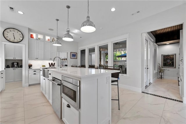 kitchen featuring sink, a breakfast bar, white cabinetry, an island with sink, and decorative light fixtures