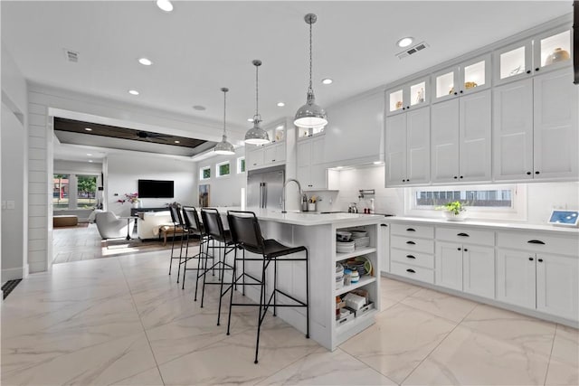 kitchen with a breakfast bar area, hanging light fixtures, stainless steel built in fridge, a kitchen island with sink, and white cabinets