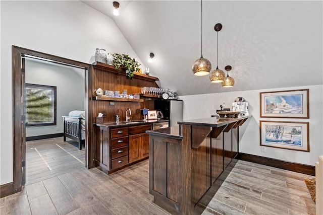 bar featuring dark brown cabinetry, sink, vaulted ceiling, light wood-type flooring, and pendant lighting