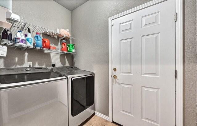 clothes washing area with light tile patterned floors, baseboards, a textured wall, laundry area, and washing machine and dryer