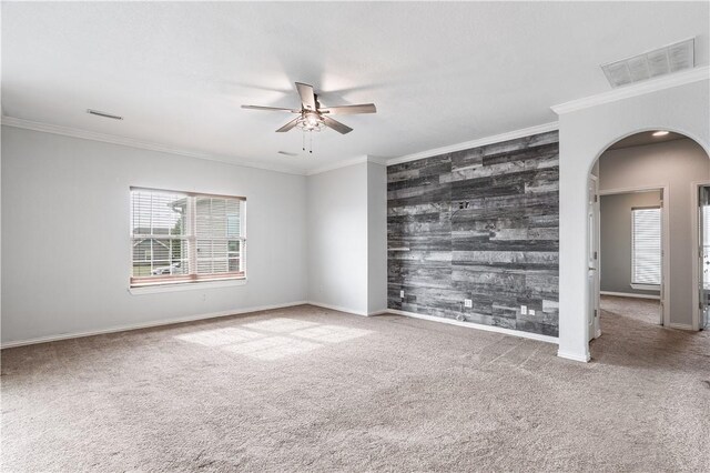 carpeted spare room with visible vents, arched walkways, ornamental molding, and an accent wall