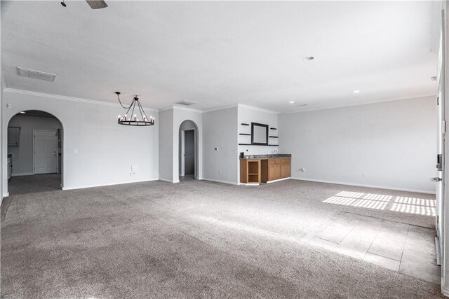 unfurnished living room featuring visible vents, ornamental molding, arched walkways, carpet flooring, and baseboards