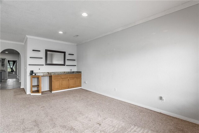 kitchen featuring baseboards, arched walkways, a sink, crown molding, and light colored carpet