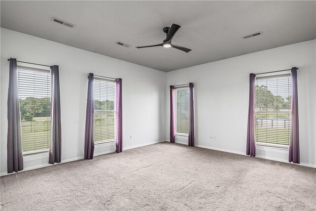 unfurnished room with a wealth of natural light, visible vents, ceiling fan, and carpet flooring
