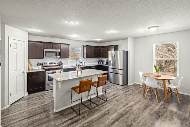 kitchen featuring a textured ceiling, stainless steel appliances, light stone counters, a center island, and hardwood / wood-style flooring