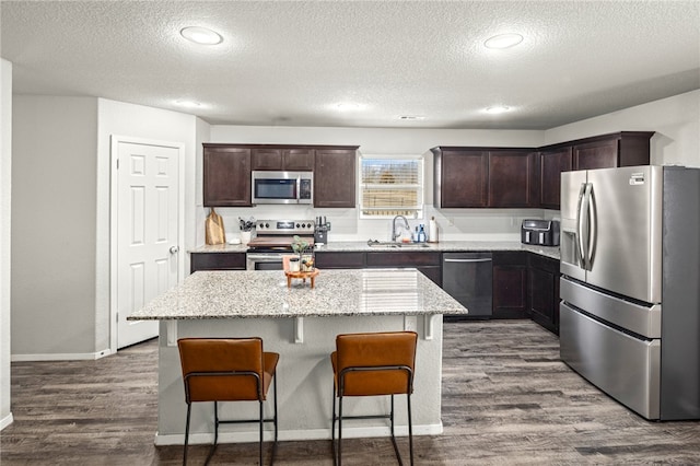 kitchen featuring a textured ceiling, a kitchen island, stainless steel appliances, sink, and wood-type flooring