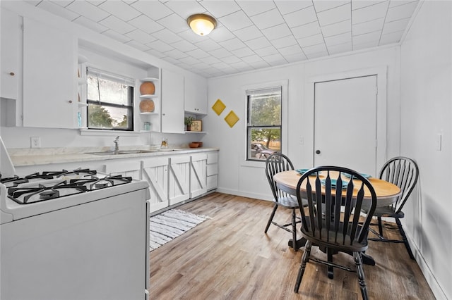 kitchen with light hardwood / wood-style flooring, white cabinets, white range with gas stovetop, and sink