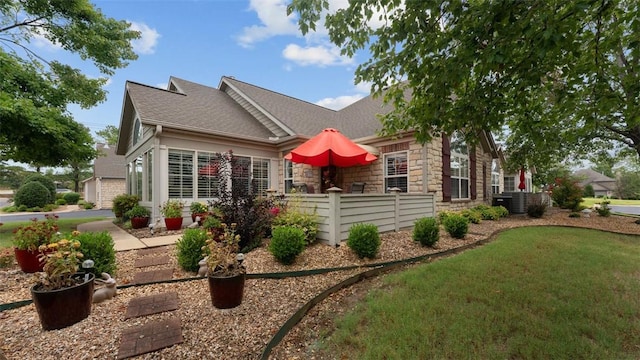 view of front facade featuring stone siding, a shingled roof, fence, and a front yard