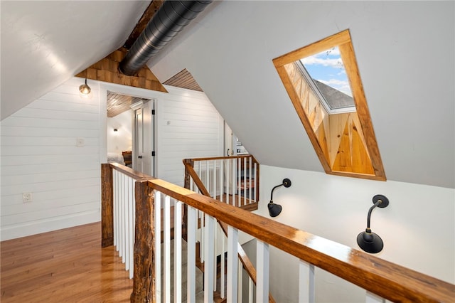 hallway with vaulted ceiling with skylight, wood walls, wood finished floors, and an upstairs landing