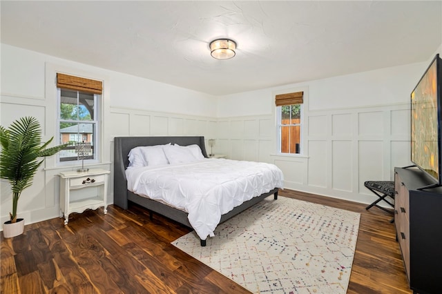 bedroom featuring a wainscoted wall, dark wood finished floors, and a decorative wall