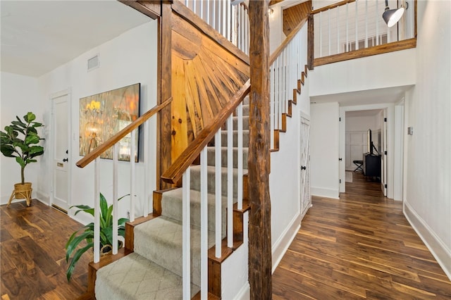 stairway with a towering ceiling, baseboards, visible vents, and wood finished floors