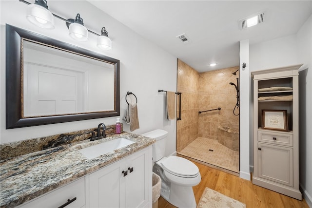 bathroom featuring vanity, toilet, a tile shower, and wood-type flooring