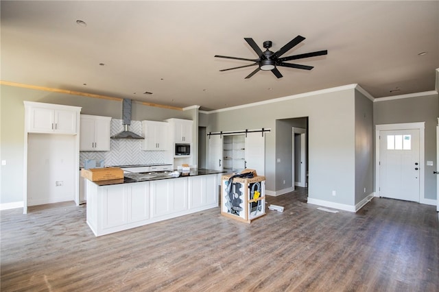 kitchen with wall chimney exhaust hood, built in microwave, crown molding, hardwood / wood-style flooring, and white cabinetry