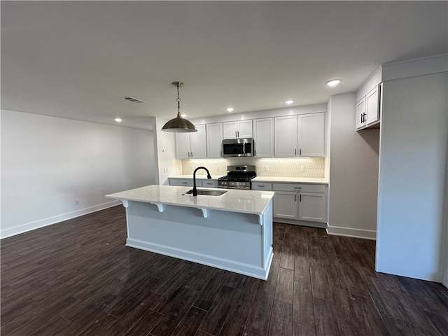 kitchen with a kitchen island with sink, sink, hanging light fixtures, dark hardwood / wood-style floors, and stainless steel appliances