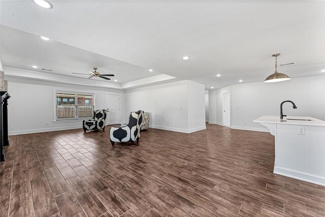 living area with visible vents, dark wood-type flooring, baseboards, a raised ceiling, and a ceiling fan