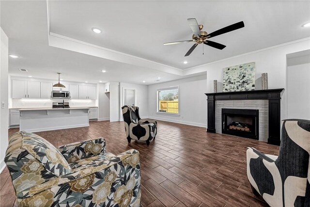 living area with wood finish floors, ornamental molding, a fireplace, baseboards, and ceiling fan