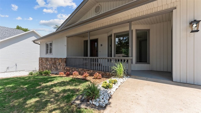 view of exterior entry featuring a lawn and covered porch