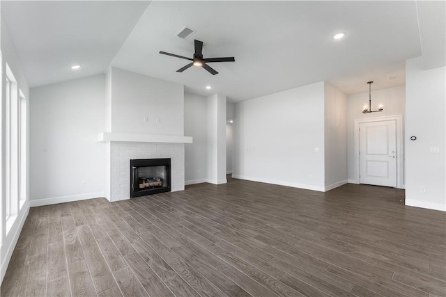 unfurnished living room with visible vents, dark wood-type flooring, a brick fireplace, vaulted ceiling, and ceiling fan with notable chandelier