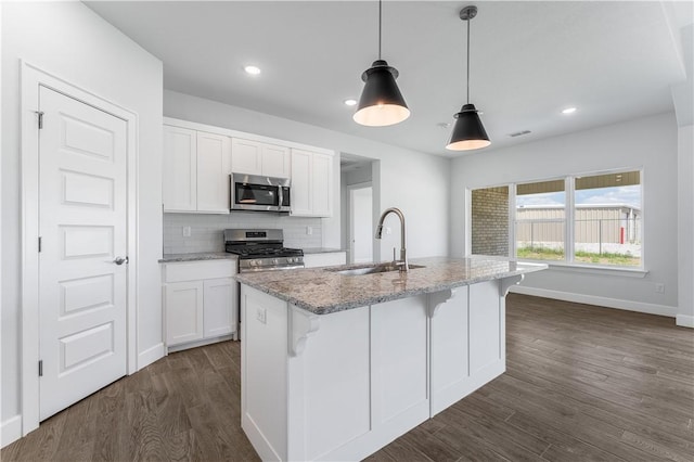 kitchen featuring white cabinets, an island with sink, decorative light fixtures, stainless steel appliances, and a sink