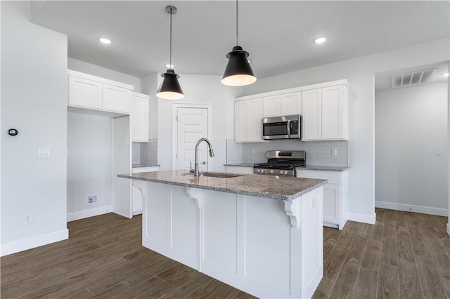 kitchen with stainless steel appliances, white cabinets, hanging light fixtures, light stone countertops, and a center island with sink