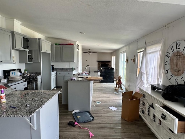 11121 Wolf Track Rd, Summers, AR 72769 - kitchen with a sink, a stone fireplace, black range, an island with sink, and ceiling fan