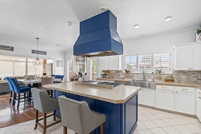 kitchen featuring white cabinetry, stainless steel gas stovetop, a kitchen island, sink, and island range hood