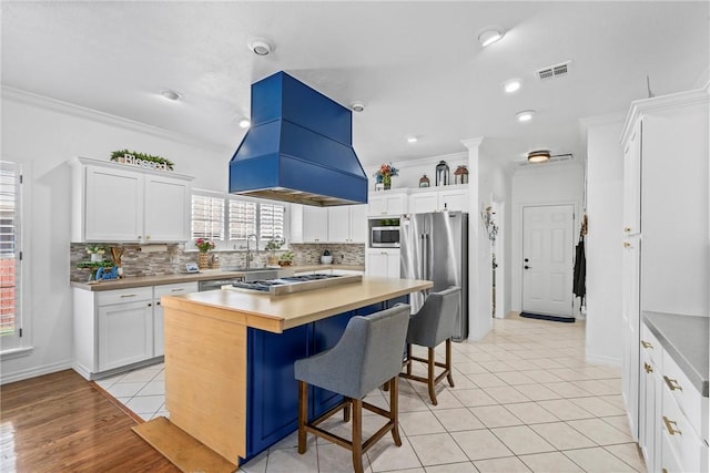 kitchen with appliances with stainless steel finishes, a center island, island range hood, white cabinets, and a breakfast bar area