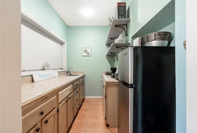kitchen with light tile patterned floors, sink, stainless steel fridge, and tile counters