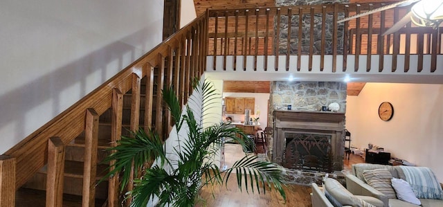 living area with a fireplace, a towering ceiling, a ceiling fan, and wood finished floors