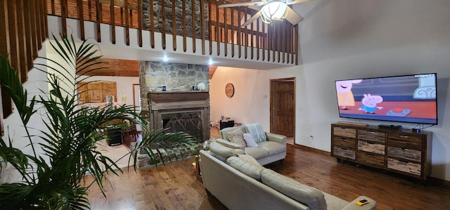 living room with hardwood / wood-style flooring, a stone fireplace, a high ceiling, and ceiling fan