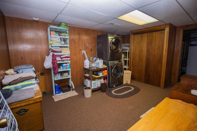 basement featuring a drop ceiling, wooden walls, carpet, and stacked washer / dryer