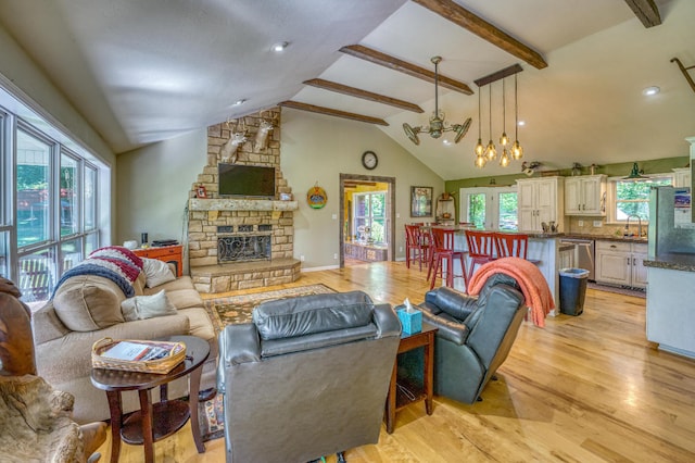 living room featuring lofted ceiling with beams, a stone fireplace, sink, light hardwood / wood-style flooring, and ceiling fan