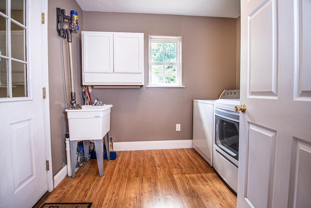 laundry room featuring cabinets, light hardwood / wood-style floors, a textured ceiling, and washer and clothes dryer