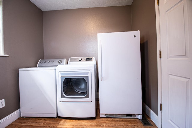 washroom with light wood-type flooring, a textured ceiling, and washing machine and dryer