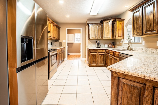 kitchen with appliances with stainless steel finishes, a textured ceiling, light tile patterned floors, light stone countertops, and sink