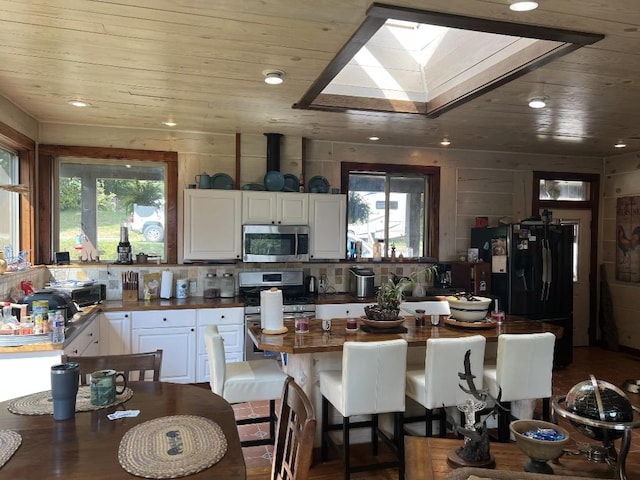 kitchen featuring white cabinets, wooden walls, a kitchen breakfast bar, and black refrigerator