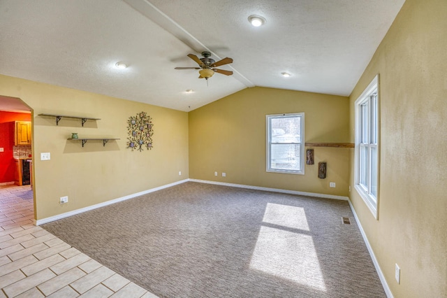 unfurnished room featuring ceiling fan, vaulted ceiling, light tile patterned flooring, and a textured ceiling